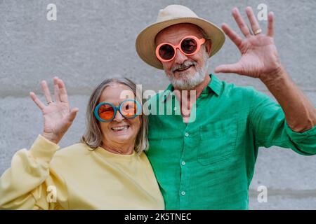 Portrait d'un couple heureux d'aînés dans des vêtements colorés agitant à l'appareil photo. Banque D'Images