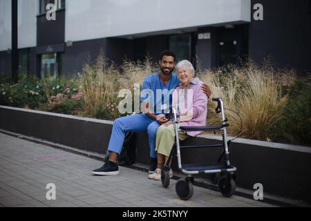 Heureuse femme âgée assise et parlant avec un assistant médical devant la maison nourissante. Banque D'Images