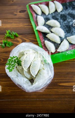 Boulettes de pâte verte crue avec persil, aneth. Boulettes crues dans un sac sur une table en bois. Banque D'Images