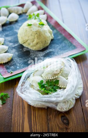 Boulettes de pâte verte crue avec persil, aneth. Boulettes crues dans un sac sur une table en bois. Banque D'Images