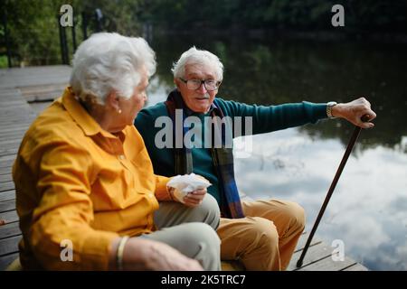 Joyeux couple senior dans des vêtements d'automne après une pause près du lac après la marche. Banque D'Images