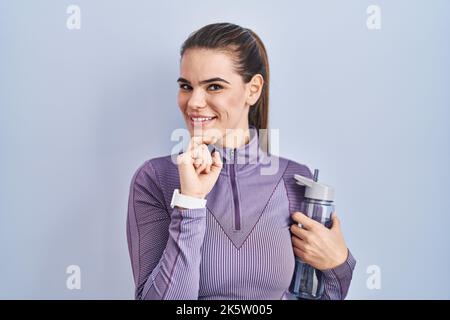 Belle femme portant des vêtements de sport tenant une bouteille d'eau avec la main sur le menton en pensant à la question, l'expression pensive. Visage souriant et réfléchi Banque D'Images