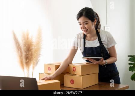 Démarrage de petites entreprises propriétaires de PME femmes entrepreneurs utilisant la tablette, recevoir et examiner des commandes en ligne pour se préparer à emballer des boîtes, vendre à des clients Banque D'Images