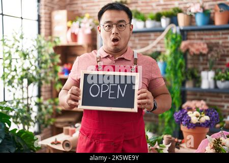 Jeune homme chinois travaillant au fleuriste tenant le signe ouvert peur et choqué avec la surprise et l'expression stupéfaite, la peur et le visage excité. Banque D'Images