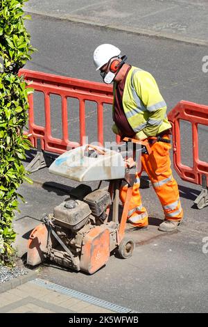 Homme travaillant bruyant poussière disque découpe scie sur le court câble large bande de dérivation pour connexion à domicile vêtements haute visibilité masque oreille défenseurs Royaume-Uni Banque D'Images