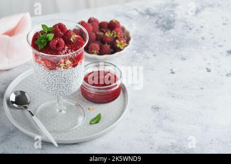 Pudding au Chia. Pudding sain au chia de vanille dans un verre avec des framboises fraîches et de la menthe sur fond blanc. Petit déjeuner sain végétalien. Banque D'Images