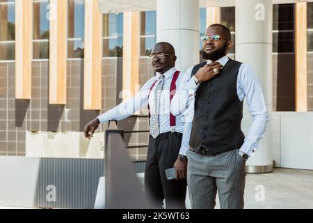 Portrait de deux hommes d'affaires à la peau sombre qui parlent en arrière-plan d'un bâtiment moderne extérieur. Réunion à l'extérieur Banque D'Images