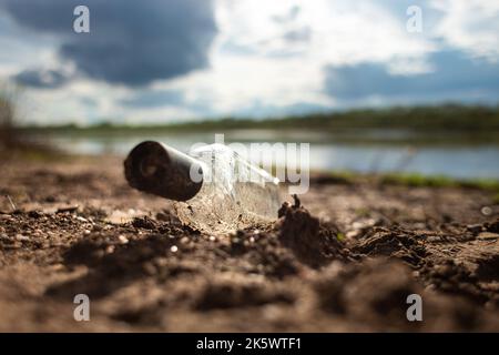 Les ordures abandonnées dans la nature. Dommages causés à l'environnement par la pollution par les ordures. Bouteille de verre gauche au milieu de l'herbe contre le fond de la rivière Banque D'Images