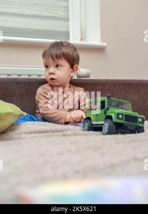 Petit garçon assis sur le lit parmi les jouets à la maison Banque D'Images
