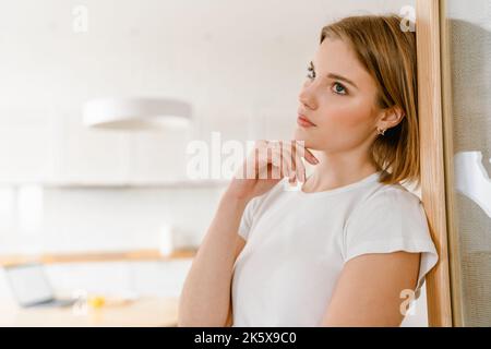 Jeune femme pensive pensive pensive penchée sur un mur dans la cuisine à la maison Banque D'Images