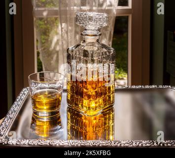 Whisky dans une bouteille en verre cristal décorée, whisky ou bourbon dans une bouteille vintage avec verre sur plateau argenté décoré dans le rétro-éclairage de la chambre Banque D'Images