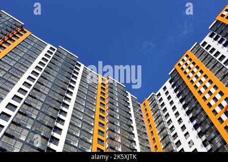 Nouveau bâtiment résidentiel avec revêtement orange et blanc contre ciel bleu. Maison avec balcons et loggias vitrés, construction en hauteur Banque D'Images