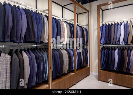 Porte-vêtements avec différents costumes pour hommes dans une boutique de vêtements pour hommes. Intérieur de marque moderne et tendance du magasin de vêtements pour hommes. Banque D'Images