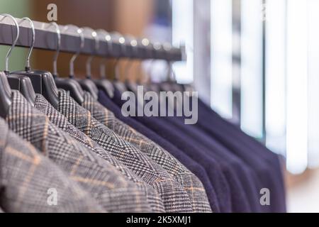 Porte-vêtements avec différents costumes pour hommes dans une boutique de vêtements pour hommes. Voyants lumineux espace de copie en arrière-plan. Banque D'Images