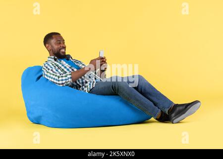 Black Homme utilisant un téléphone portable assis dans la chaise Beanbag dans le studio Banque D'Images