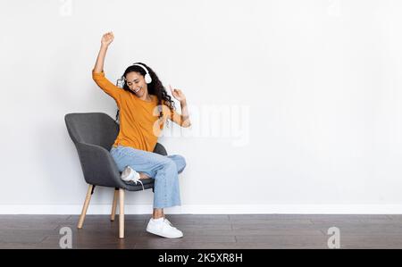 Jeune femme joyeuse assise dans un fauteuil, à l'écoute de musique Banque D'Images