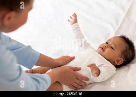 Maman qui s'occupe faire un massage pour un bébé noir mignon allongé sur le lit Banque D'Images