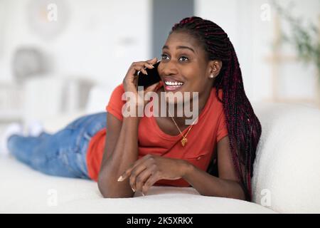 Joyeuse Black Lady parlant au téléphone portable et se détendant sur le canapé à la maison Banque D'Images