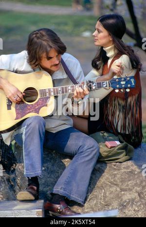 Jeune femme adulte écoutant un jeune homme adulte jouant de la guitare acoustique, Central Park, New York City, New York, États-Unis, Toni Frissell Collection, mai 1970 Banque D'Images