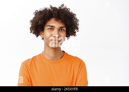 Gros plan d'un beau garçon mauri avec piercing, un homme queer dans un t-shirt orange souriant, debout sur fond blanc Banque D'Images