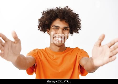 Portrait en gros plan d'un homme hispanique souriant, qui se tend les mains, qui s'étire les bras, tient quelque chose, se tenant sur un fond blanc Banque D'Images