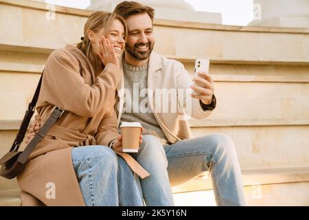 Couple romantique blanc riant et prenant le selfie sur le téléphone portable pendant la date à l'extérieur Banque D'Images