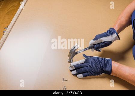 Vue rapprochée des mains de l'homme avec un marteau pour assembler les nouveaux meubles. Banque D'Images