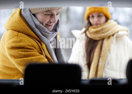 Gros plan sur un homme adulte souriant qui décharmera le coffre de sa voiture en hiver lors d'un voyage en famille pour Noël Banque D'Images