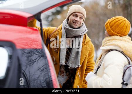 Portrait d'un jeune couple souriant debout en voiture arrivant pour les vacances d'hiver Banque D'Images