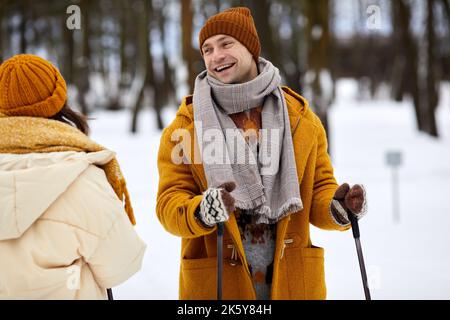 Portrait de couple heureux skier en forêt d'hiver, concentrez-vous sur un jeune homme insouciant avec des bâtons de ski souriant à la petite amie Banque D'Images