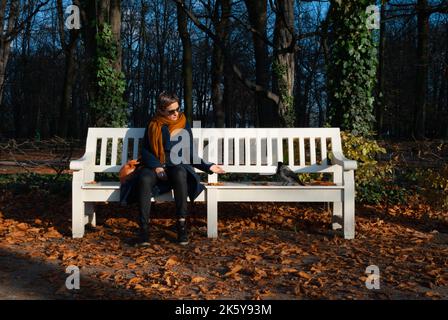 Une femme nourrit une corbeau avec sa main assise sur un banc de parc Banque D'Images