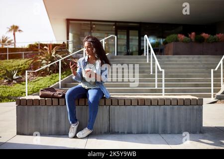 Femme souriante utilisant un smartphone assis sur un banc Banque D'Images