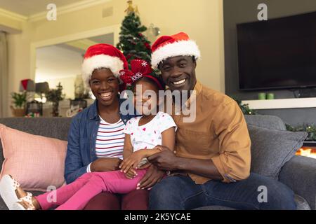 La famille afro-américaine porte des chapeaux de père noël assis sur le canapé Banque D'Images