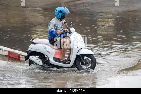 SAMUT PRAKAN, THAÏLANDE, OCT 04 2022, Un homme sur une moto conduit à travers une flaque sur une rue de ville Banque D'Images