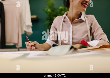 Coupe courte d'une femme asiatique travaillant dans son studio. Créateur de mode assis à table et faisant de nouveaux motifs de robe. Banque D'Images
