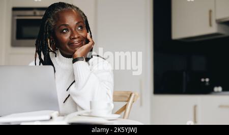 Femme d'affaires mûre regardant loin avec soin tout en travaillant sur un ordinateur portable à la maison. Femme d'affaires senior travaillant en ligne freelance dans son bureau à domicile. Banque D'Images