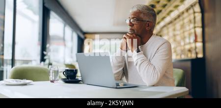 Homme d'affaires mûr regardant loin avec soin tout en travaillant dans un café moderne. Homme d'affaires senior utilisant un ordinateur portable tout en travaillant à distance. Banque D'Images