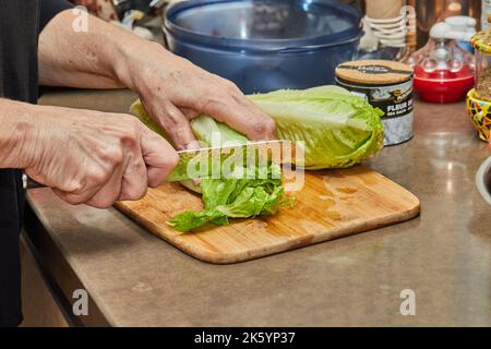 Le chef coupe de la laitue sur une planche de bois dans la cuisine Banque D'Images