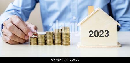 Homme d'affaires de la main mettant la pièce de monnaie dorée sur les escaliers de l'argent croissant avec 2023 maison en bois. Bonne année d'affaires, d'investissement, de planification de retraite, de finances, Banque D'Images