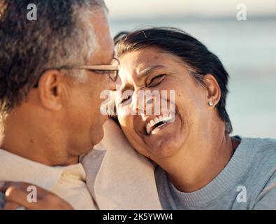Un couple de course mixte senior marchant ensemble sur la plage souriant et riant lors d'une journée à la plage. Mari et femme hispaniques regardant heureux et Banque D'Images