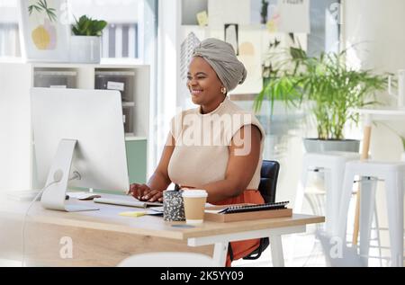 Bonne jeune femme d'affaires afro-américaine souriante en utilisant un ordinateur de bureau et assise à un bureau dans un bureau moderne. Un confiant Banque D'Images