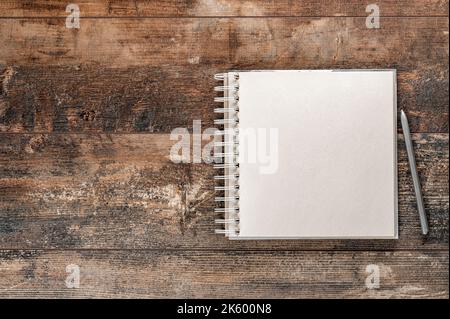 Bloc-notes ou carnet de croquis avec maquette au stylet. Vue de dessus sur un carnet marron vierge sur un arrière-plan marron ancien, sur une surface plane, sur un espace de copie. Art, artisanat, inspiration, mémoire Banque D'Images