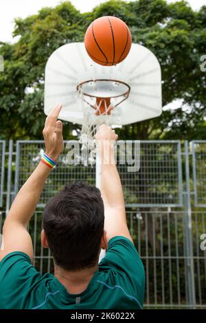Photo verticale d'un homme avec un bracelet arc-en-ciel qui jette une balle sur le panier dans un terrain de basket-ball Banque D'Images