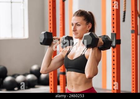 Forte athlète féminine en soutien-gorge de sport faisant de l'exercice de pression de haltères tout en s'exerçant dans la salle de gym moderne Banque D'Images