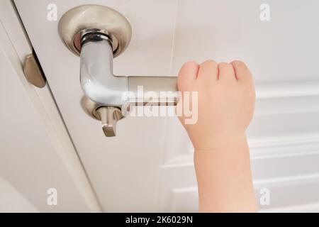 Tout-petit ouvre la porte maintenant la poignée de porte, la main de l'enfant en gros plan. Porte en bois blanc, poignée de porte en métal et main de bébé Banque D'Images