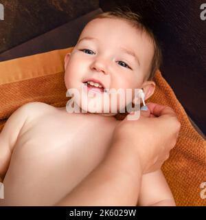 La mère nettoie l'oreille avec un coton-tige pour le bébé garçon heureux. Maman nettoie les oreilles d'un enfant souriant. Enfant d'un an Banque D'Images