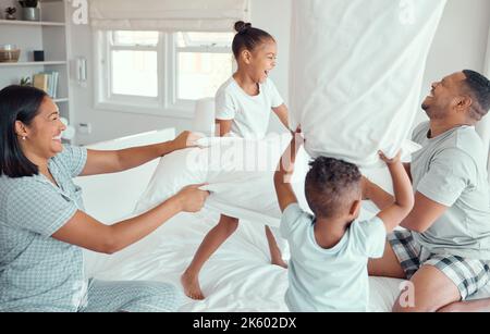 Deux enfants heureux en train de rire et de profiter de l'oreiller lutte avec les parents dans la chambre à la maison. Joyeux enfants fille et fils jouant avec la mère et le père Banque D'Images