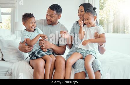 Joyeux drôle de famille de race mixte avec deux enfants portant un pyjama et assis ensemble à la maison. Parents joyeux assis dans leur chambre avec leur Banque D'Images