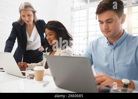 Trois hommes d'affaires différents travaillent ensemble dans un bureau au travail. Femme d'affaires mûre aidant ses collègues à travailler sur un ordinateur. Jeunes africains Banque D'Images