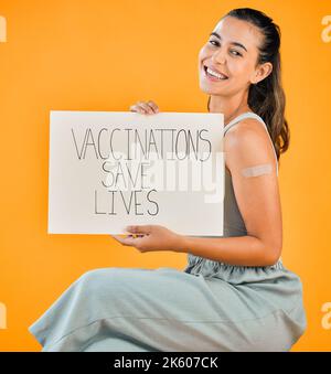 Race mixte covid vaccinée femme montrant du plâtre sur le bras et tenant l'affiche. Portrait d'une femme hispanique souriante isolée contre un studio jaune Banque D'Images